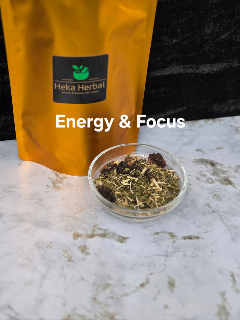 A gold stand-up pouch labeled Heka Herbal stands on a white marble surface next to a small clear bowl filled with loose herbal tea. White text across the center reads 'Energy & Focus'.
