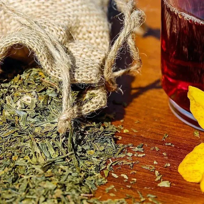 Heka Herbal natural bath soak for tension with dried herbs spilling from a burlap pouch next to a glass of red liquid